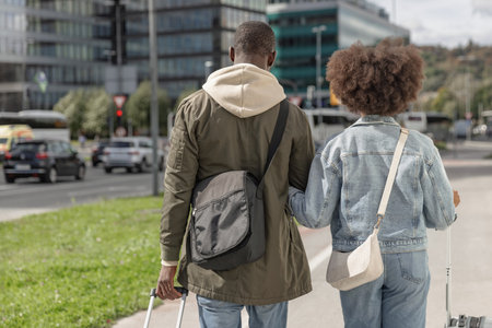 Tourist couple rolling their suitcases along a city street on their way to the modern hotel...