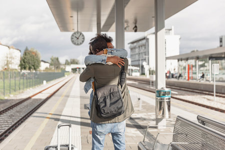 Happy young African American couple hugging at a train station, meeting after a long journey. Travel, welcome, and love concepts.の写真素材