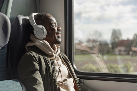 Smiling African American man enjoying relaxing and comfortable train travel, sitting by a window,...