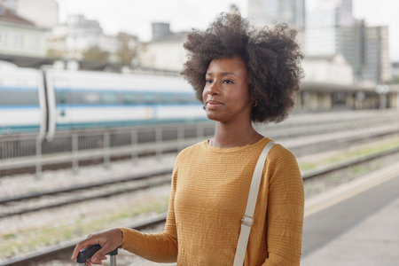 African American woman waiting for a train on a railway station platform. Solo traveling lifestyles concept.の写真素材
