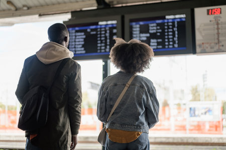Two passengers, an African American couple looking at a train departure board on a railway station. Travel and tourism concepts.の写真素材