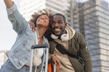 African American tourist couple having fun taking selfies on a busy European city street with modern skyscraper architecture.の写真素材