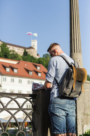 Male tourist with a backpack standing on the street route for pedal cycles and pedestrians and looking at the city map. Travel and experience concepts.の写真素材