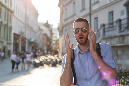 Shocked stunned young man, with sunglasses and a backpack, grabbing his head and looking at the...