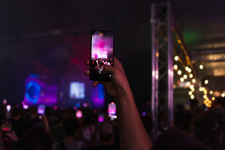 Person holding smartphone at concert crowd with stage laser lightsの写真素材