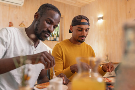 Two African American LGBT couple having breakfast, tasting fresh fruit and vegetables, enjoying delicious healthy food taste in a hotel accommodation.の写真素材