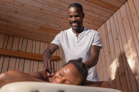 Young African American woman with a tranquil smile during a relaxing massage, close up shot. Self-care, health, and wellbeing concepts.の写真素材