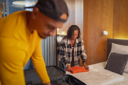 African American man preparing for a trip while his girlfriend helps him pack a suitcase in a bedroom. Traveler lifestyles concepts.の写真素材