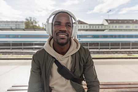 African American man waiting for a train on a railway station platform. Solo traveling lifestyles...