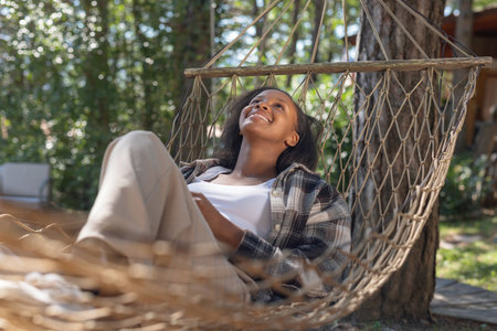 Carefree African American woman enjoying a resort trip, relaxing in a hammock. Nature connection, and vacation concepts.の写真素材