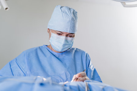 Female veterinary surgeon suturing the wound after dog cancerous tumor removal procedure in an animal hospital operating room.の写真素材