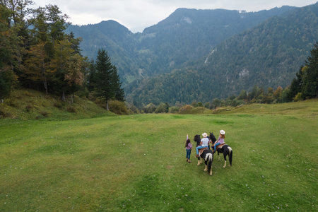 Couple on horseback, guided by instructors at a western riding school, pausing to take the breathtaking panoramic view of the surrounding mountains, aerial shot.の写真素材