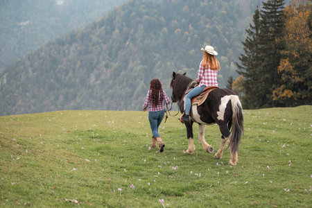 Woman rider mounts her horse, preparing for a journey through the serene landscape of the ranch riding school, accompanied by a cowgirl instructorの写真素材