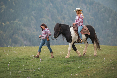 Girl on a horse ride adventure in misty mountains, horseback lesson in scenic nature setting at riding school with experienced cowgirl instructorの写真素材