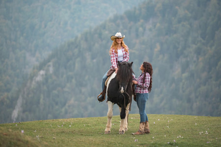 Woman rider mounts her horse, preparing for a journey through the serene landscape of the ranch riding school, accompanied by a cowgirl instructorの写真素材