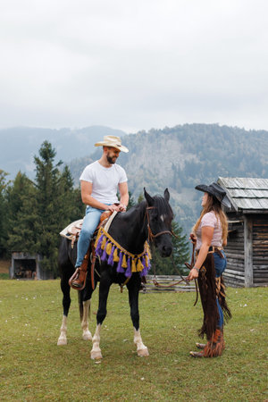 Cowgirl instructor, holding the reins, watching and helping a young rider mount his horse at the ranch riding schoolの写真素材