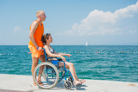 Smiling woman with a disability and her assistant helping her wheelchair move, enjoying time at the...
