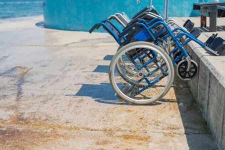 Empty blue steel wheelchair, for people with disabilities, placed on the sea dock, enabling access to the beautiful seaside environment.の写真素材