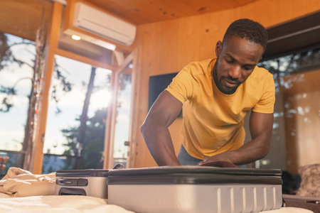 African American man packing and zipping his suitcase, ready to leave a hotel room. Travel, and departure concepts.の写真素材