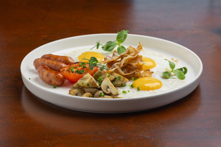 A delicious brunch breakfast platter showcases sunny-side-up eggs, sausages, mushrooms, and grilled tomato on a white plate, perfect for morning energy.の写真素材
