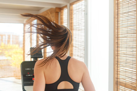 A woman jogs on a treadmill indoors, her hair flowing freely as she enjoys a workout in bright, natural light.の写真素材