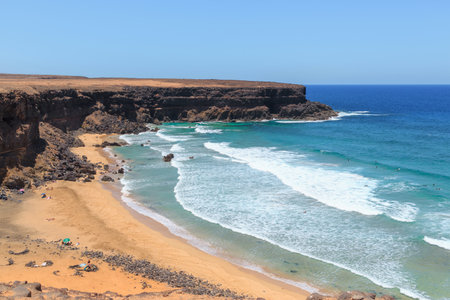 Waves crash on the sandy shores of Fuerteventura, where sunbathers enjoy the warm weather and surfers catch the perfect waves.の写真素材