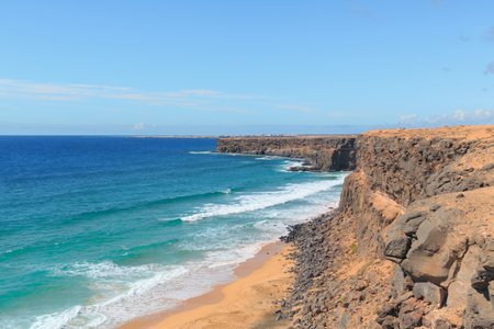 Dramatic cliffs overlook the turquoise waters and sandy beaches of Fuerteventura in the Canary Islands on a clear sunny day.の写真素材