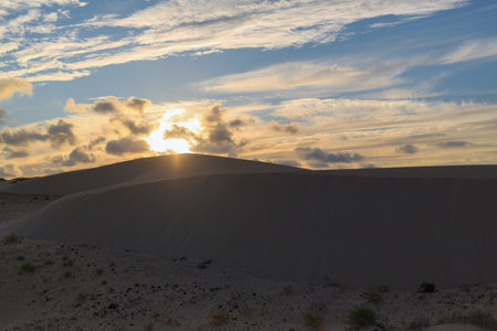 The sun sets behind majestic sand dunes in Fuerteventura, casting a warm glow and creating a tranquil atmosphere during the evening.の写真素材