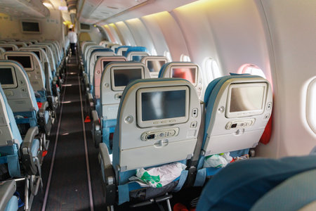 Rows of blue seats fill the airplane cabin, with overhead lights dimmed. Passengers prepare for...