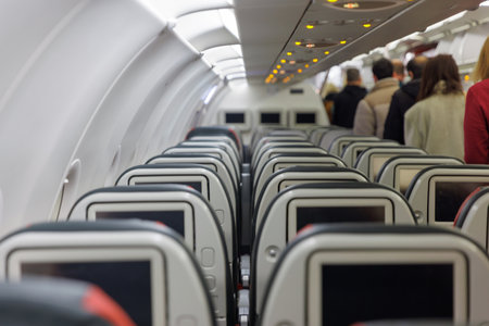 A crowded airport terminal shows passengers lining up to board a plane. The interior features rows of empty seats with personal screens, highlighting travel excitement.の写真素材