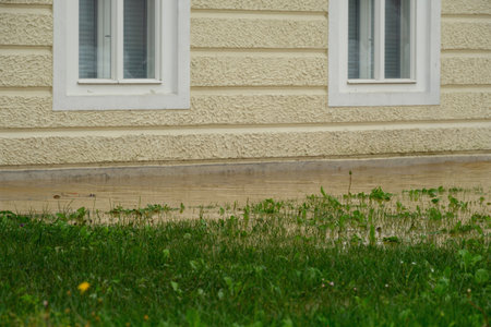 Heavy rainfall has caused significant flooding near a residential building, with waters encroaching upon the grassy area and foundation.の写真素材
