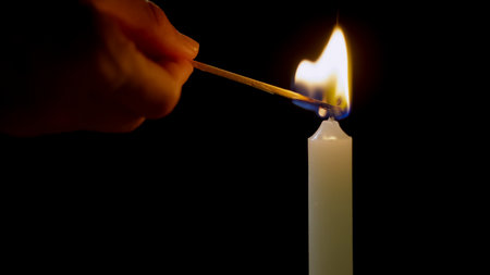 A hand is using a match to ignite a mourning candle wick in a dark setting, creating a warm and flickering flame.の写真素材