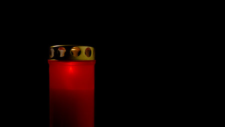 A red mourning cemetery candle stands against a black background, casting a warm glow and creating a peaceful atmosphere in the darkness.の写真素材