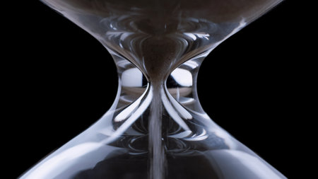 Fine sand flows steadily through the narrow neck of a transparent hourglass.