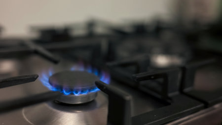 Blue flames emit from a gas stove burner, illuminating a kitchen workspace with a warm glow.