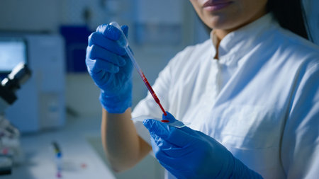A lab technician uses a pipette to transfer blood samples onto a slide for analysis in a modern...