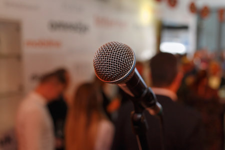 A close-up of a microphone ready for a speech, with blurred people engaging in lively conversation in the background.の写真素材