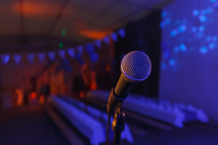 A microphone stands prominently in a dimly lit venue decorated for an upcoming event with colorful lights.の写真素材