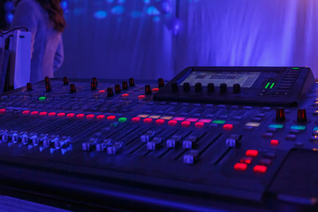 A sound mixing board illuminates with colorful lights during an event, showcasing professional audio...