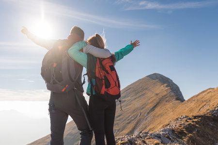A couple stands atop a mountain, embracing with joy as sunlight shines behind them.の写真素材