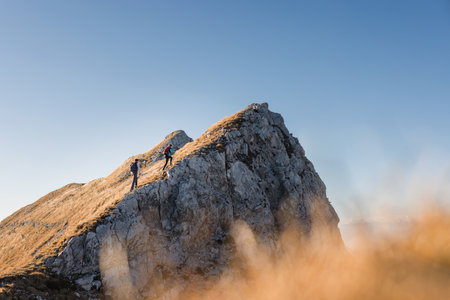 Two climbers scale a rocky peak under clear skies, capturing their adventurous spirit at golden hour.の写真素材