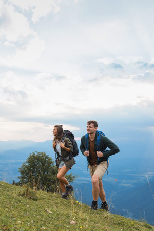Young couple with backpacks enjoying a summer hiking tour along an uphill trail to their campsite,...