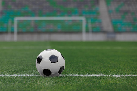 Soccer ball rests on bright green grass inside an empty stadium with seating in the background.