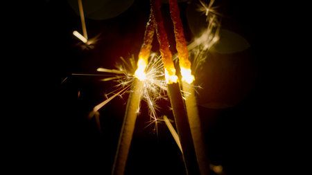 Celebration sparklers burning, making shining sparks on a festive background with golden lights,...