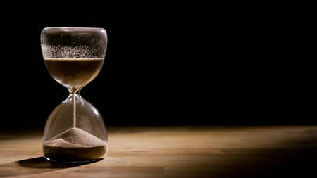Hourglass on a wooden table with a black background, sand flowing through the bulb. Time, and life...