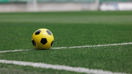 A bright yellow football lies on the lush green field, ready for play in the stadium during match...
