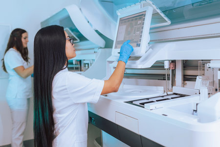 Two female medical laboratory professionals working on blood chemistry analyzers, highly specialized...