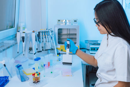 Female laboratory technician using digital electronic multichannel pipette to fill reagents during...