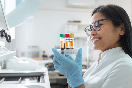 A lab technician smiles while examining blood samples in a modern laboratory setting during the day.