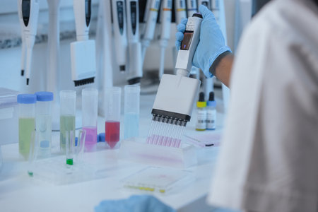 A laboratory technician uses a pipette to transfer liquids in a lab setting. Colorful tubes are arranged on the table.の写真素材